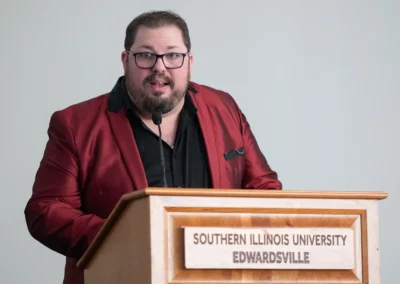 A speaker in a red blazer presents from a Southern Illinois University Edwardsville podium.